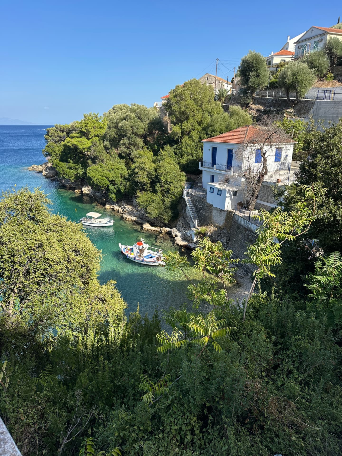 Small cove with boats in turquoise water beside a whitewashed house with blue shutters on Ithaca