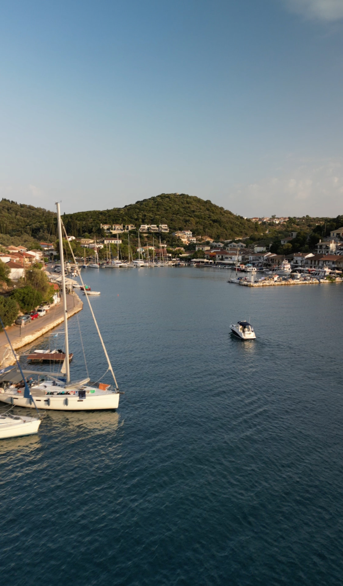 Sailboats and yachts moored in a sheltered harbour below green hills on Meganisi