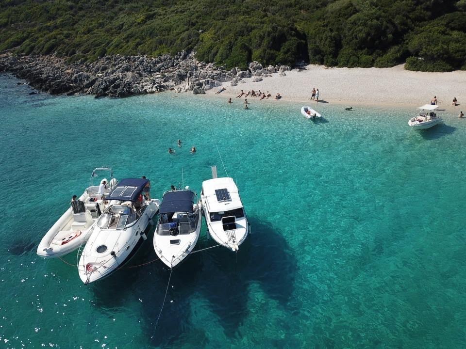 Aerial view of a secluded pebble cove with clear turquoise water and boats anchored offshore