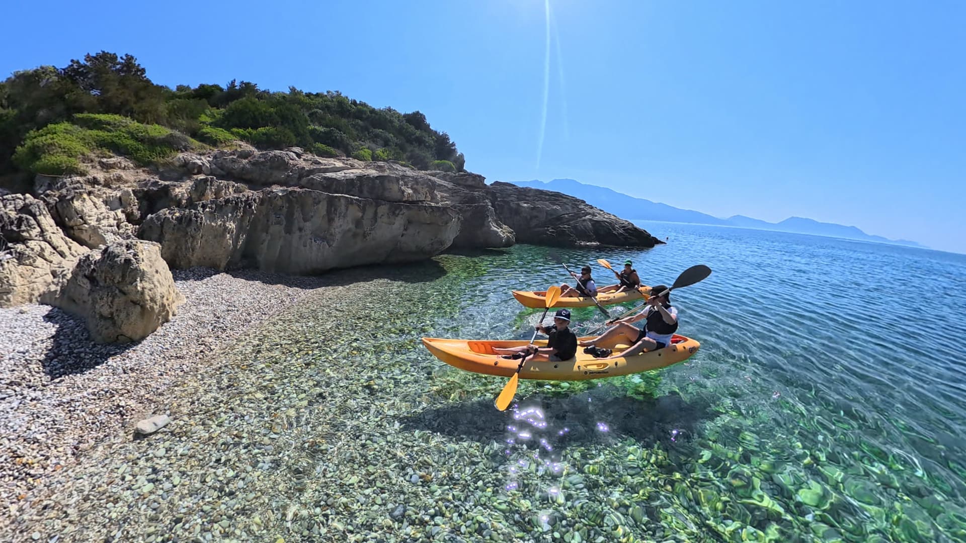 Kayaking on clear turquoise Ionian water beside a pebble beach and cliffs