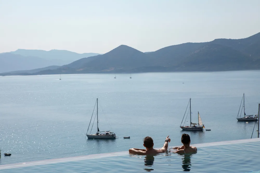 Guests in an infinity pool watching sailboats in the bay